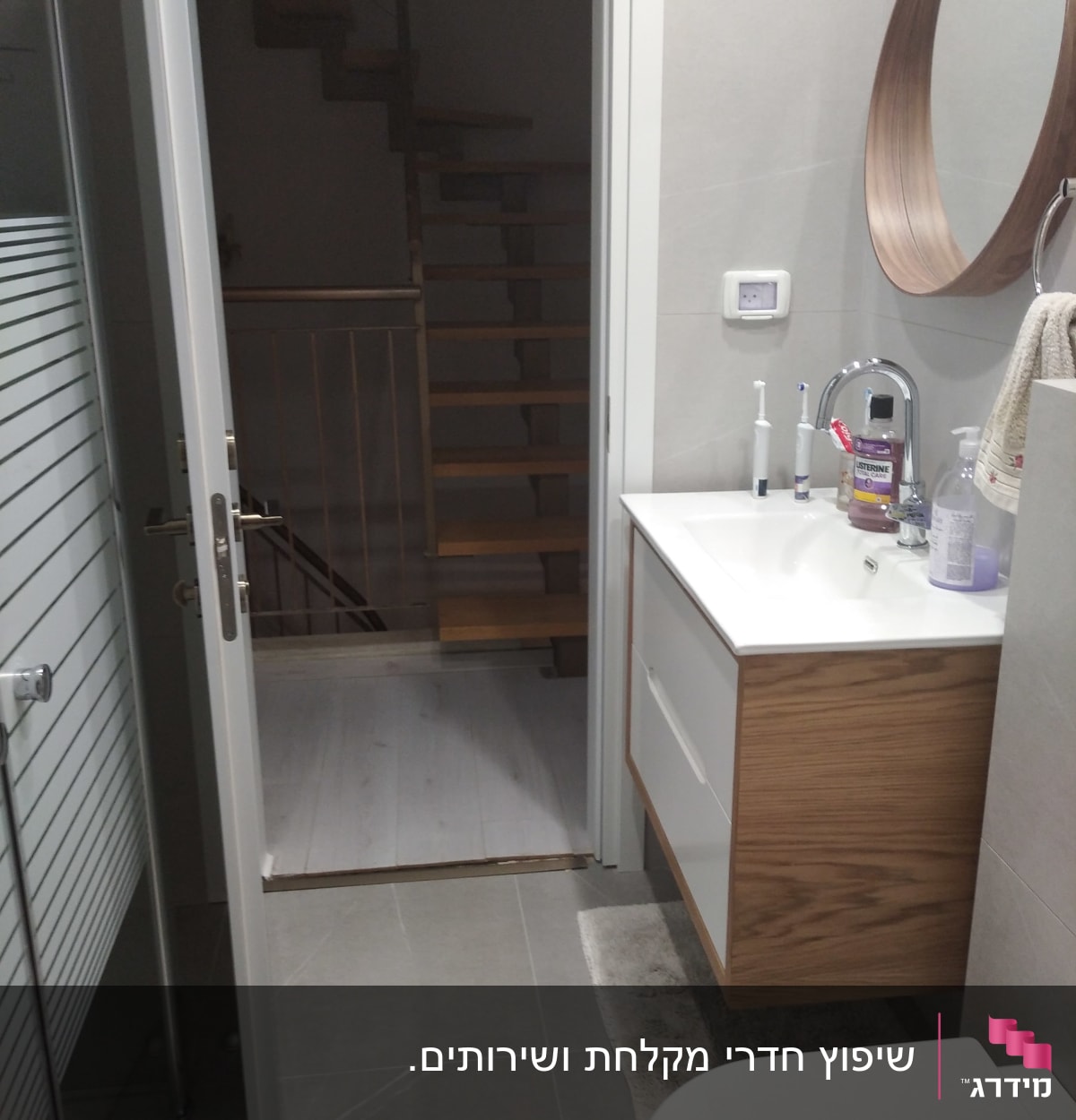 חדר אמבטיה עם כיור, מראה עגולה ודלת פתוחה למדרגות